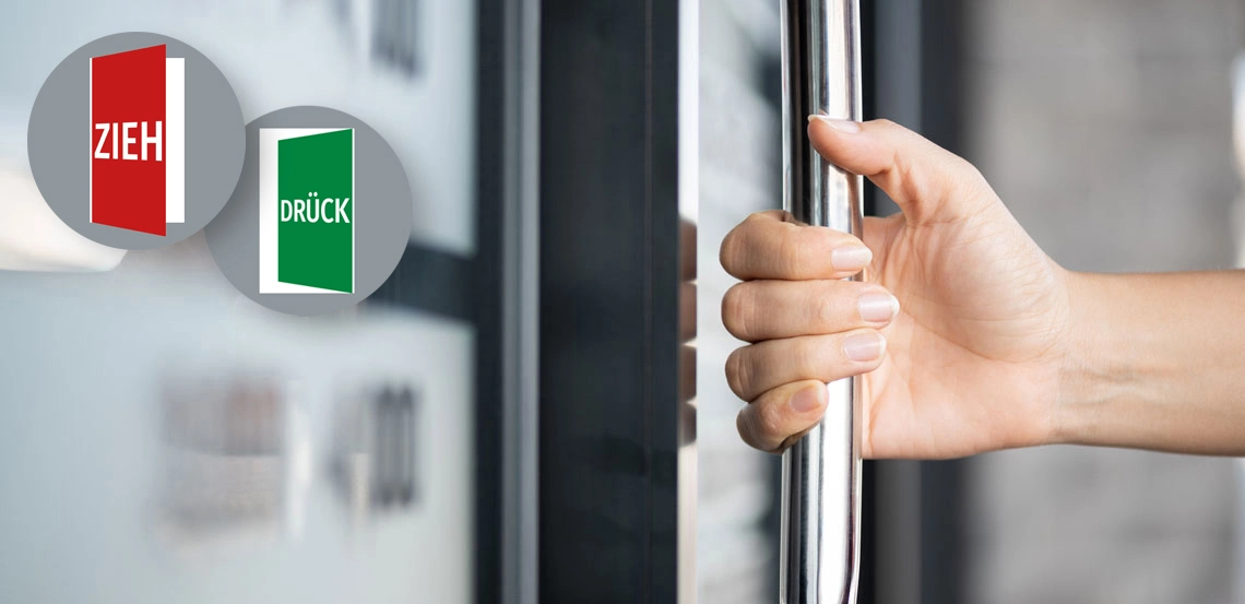 Hand öffnet eine Tür, links oben das Paar Navigadoor-Schilder - Modell Rondo links mit dem Text Zieh und Drück